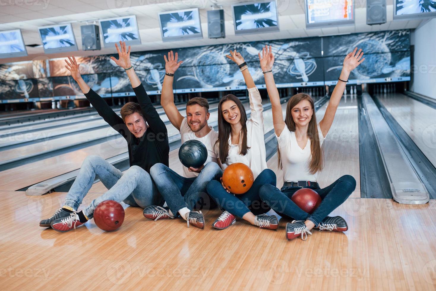 posición de victoria. jóvenes amigos alegres se divierten en el club de bolos los fines de semana foto