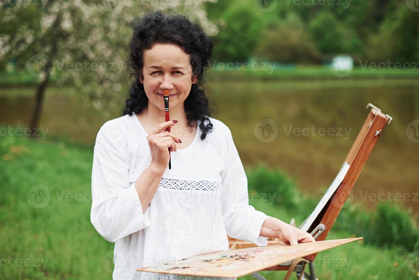 Having fun during the process. Portrait of mature painter with black curly hair in the park outdoors photo