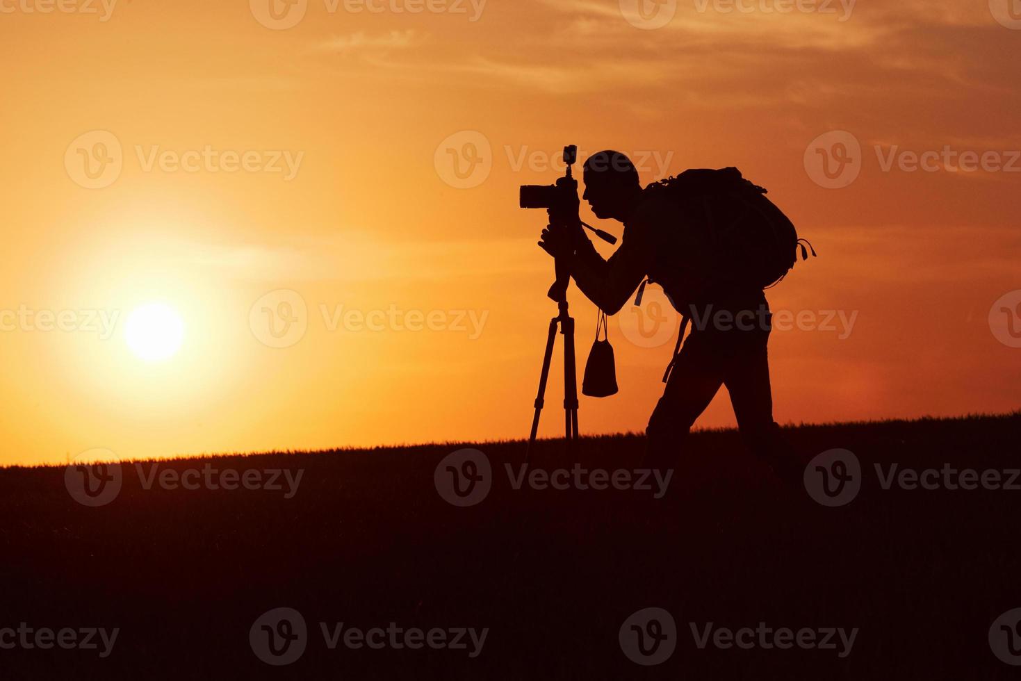 Photographer with professional equipments makes photos. Stands in the field illuminated by sunlight photo