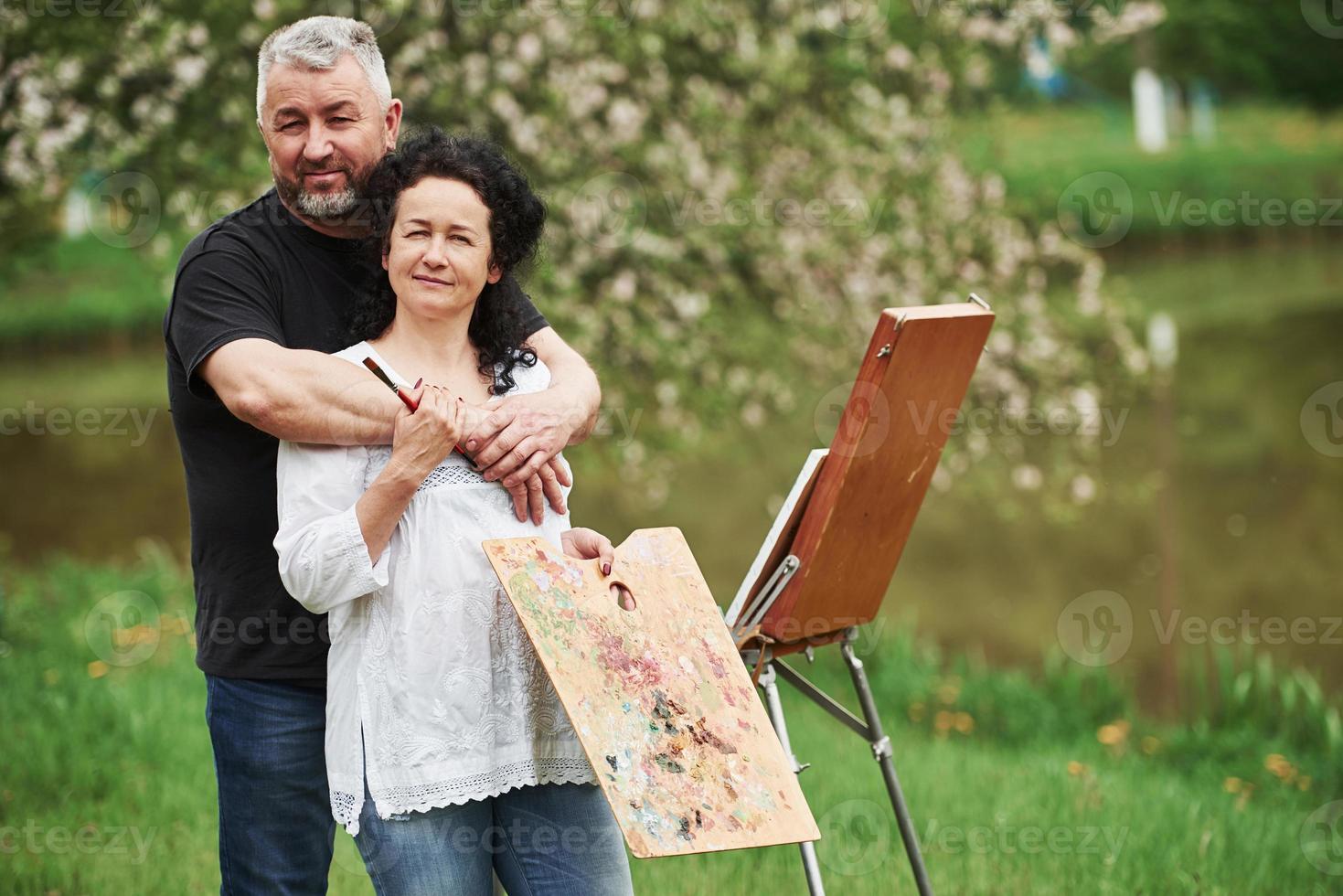 Looking into the camera. Mature couple have leisure days and working on the paint together in the park photo