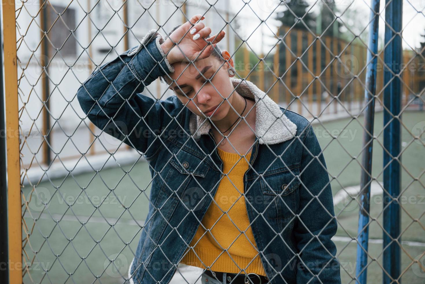 Thoughtful girl in casual clothes leaning on the fence outdoors photo