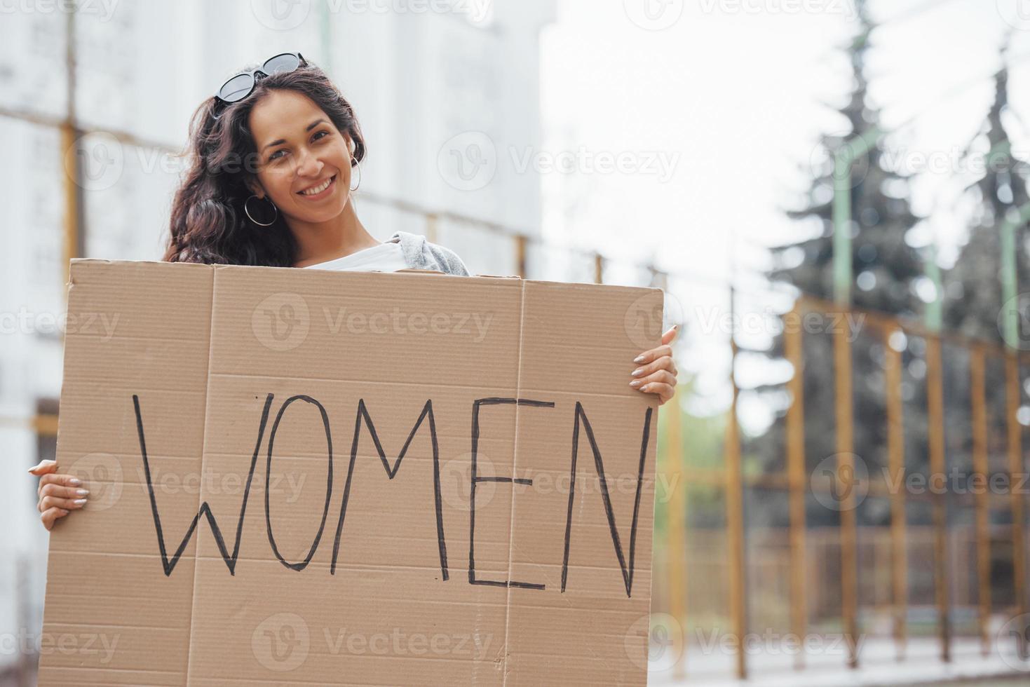 Pretty girl with curly hair stands with handmade feminist poster in hands photo