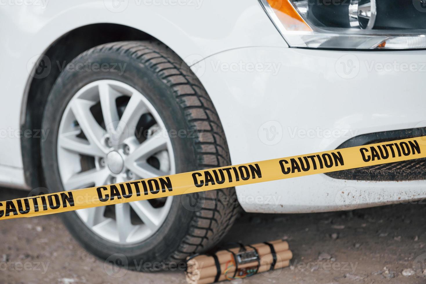 Attempt is prevented. Dangerous explosive near the wheel of modern white car. Yellow caution tape in front photo