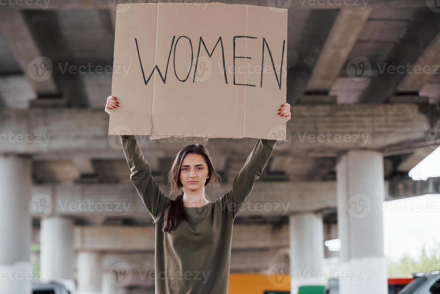 Standing alone. Pretty girl in casual clothes with handmade feminist poster in hands photo