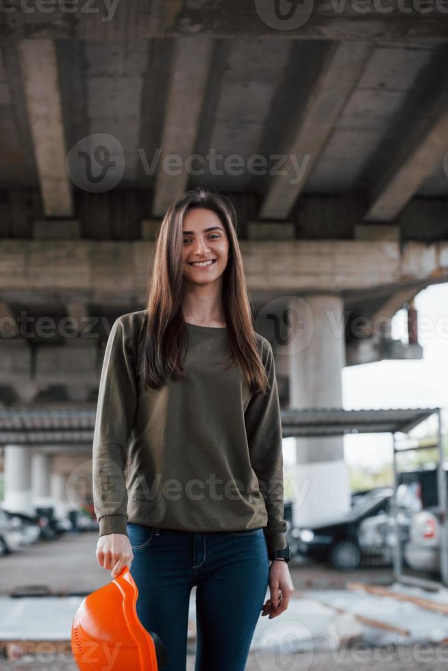 chica positiva. retrato de una hermosa joven con casco de seguridad parado debajo del puente foto