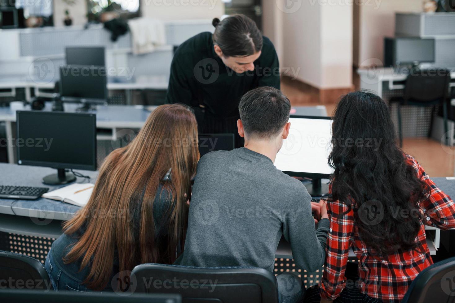 Together near one monitor. Group of young people in casual clothes working in the modern office photo