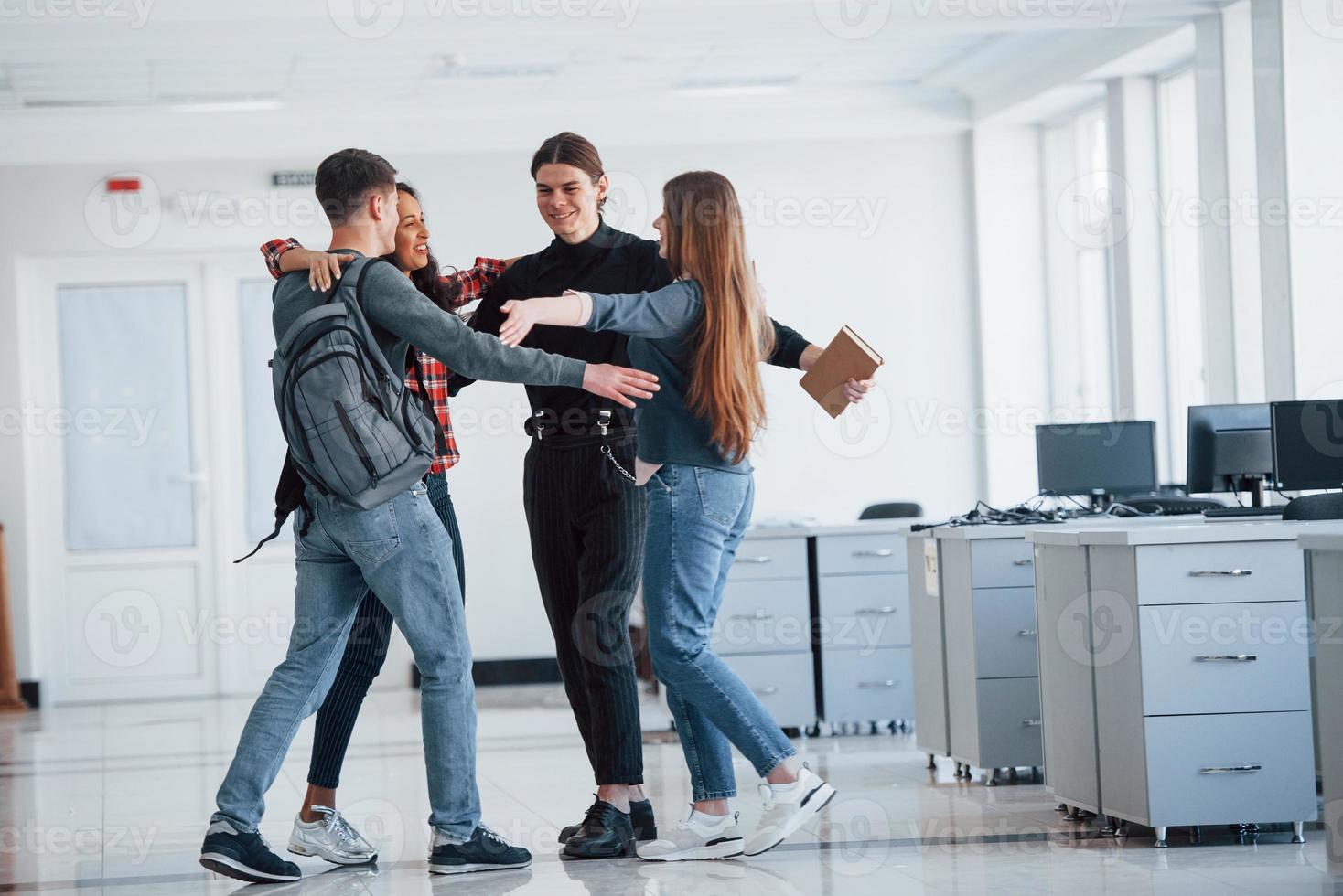 Giving hugs to each other. Group of young people walking in the office at their break time photo