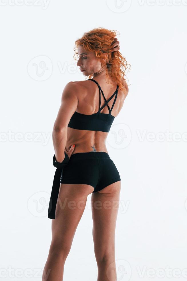 With black bandage in hand. Redhead female bodybuilder is in the studio on white background photo