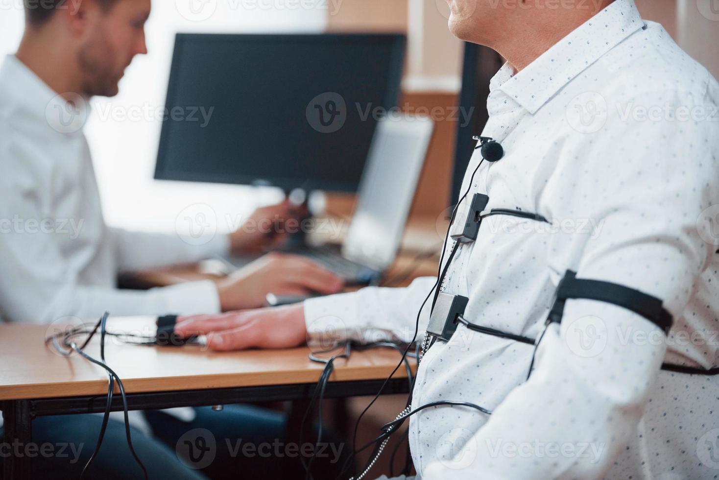 Microphone and sweating sensors. Suspicious man passes lie detector in the office. Asking questions. Polygraph test photo