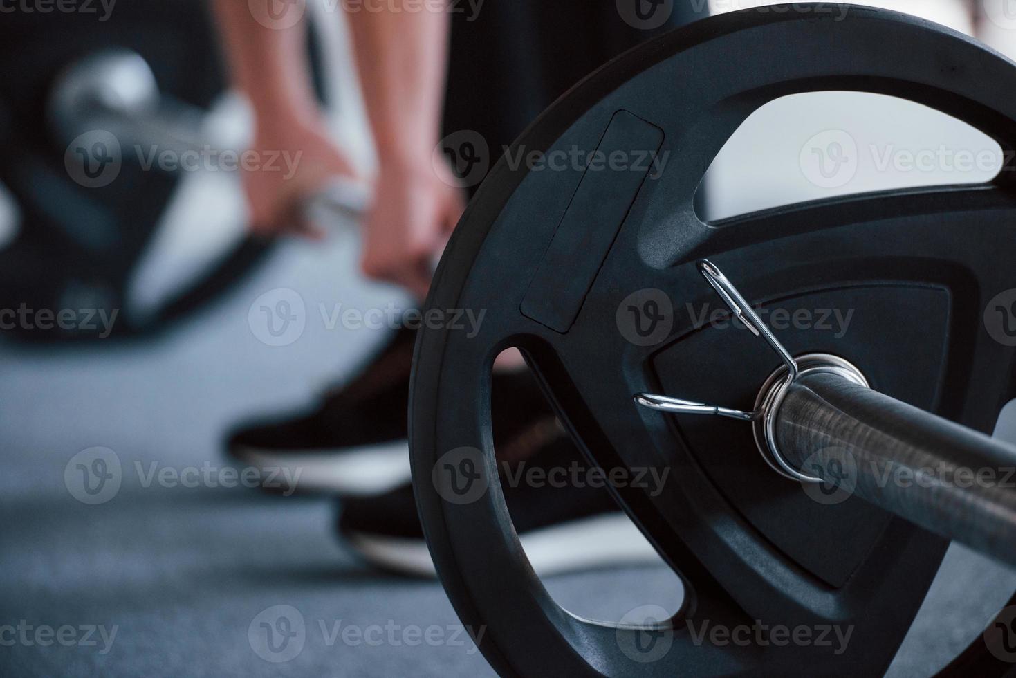 Holding the barbell. Cropped photo of woman doing squatting with barbell in the gym