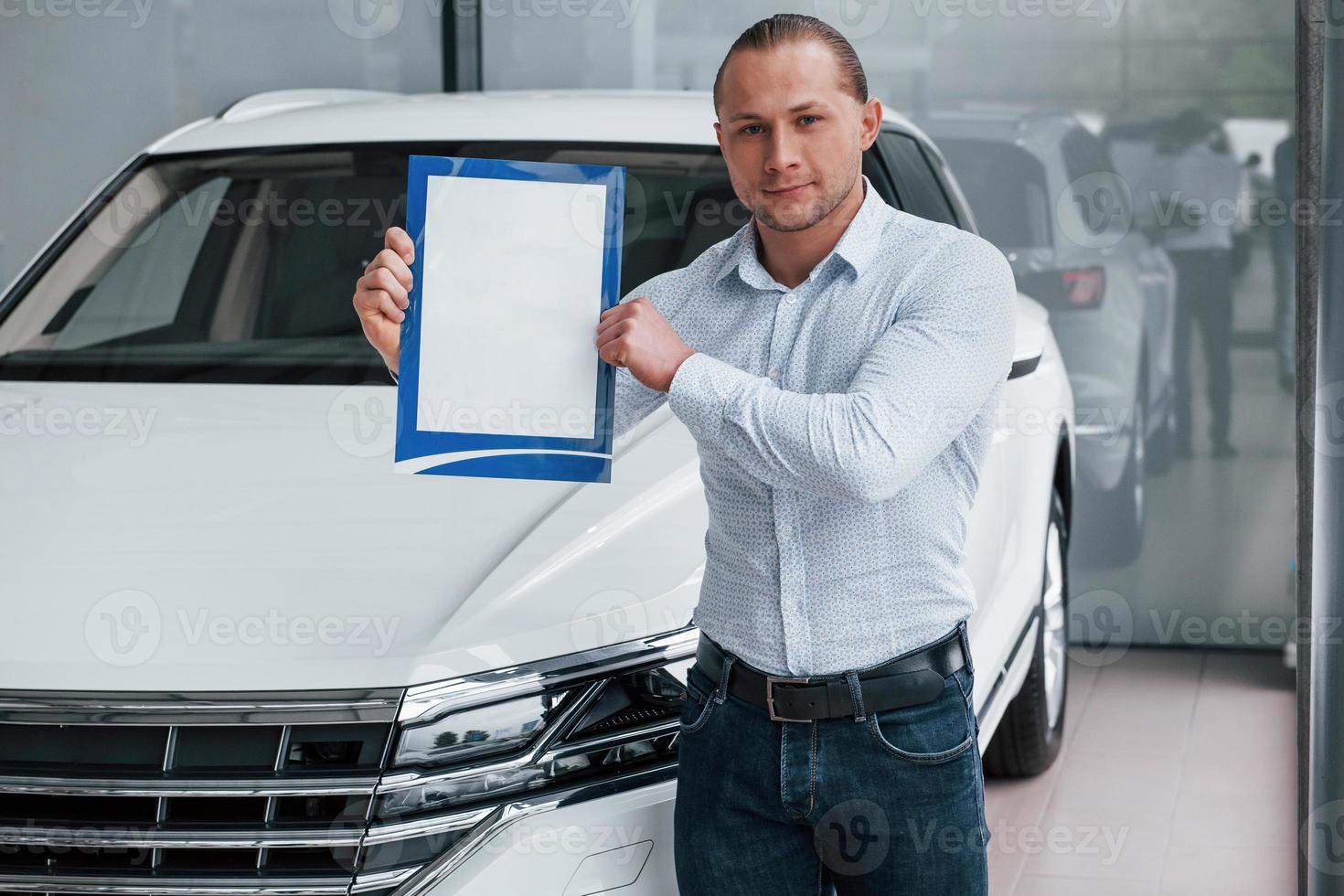 Important document. Manager stands in front of modern white car with paper in hands photo