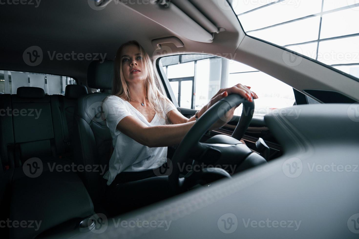 mirando en el espejo. chica en coche moderno en el salón. durante el día en el interior. compra de vehiculo nuevo foto