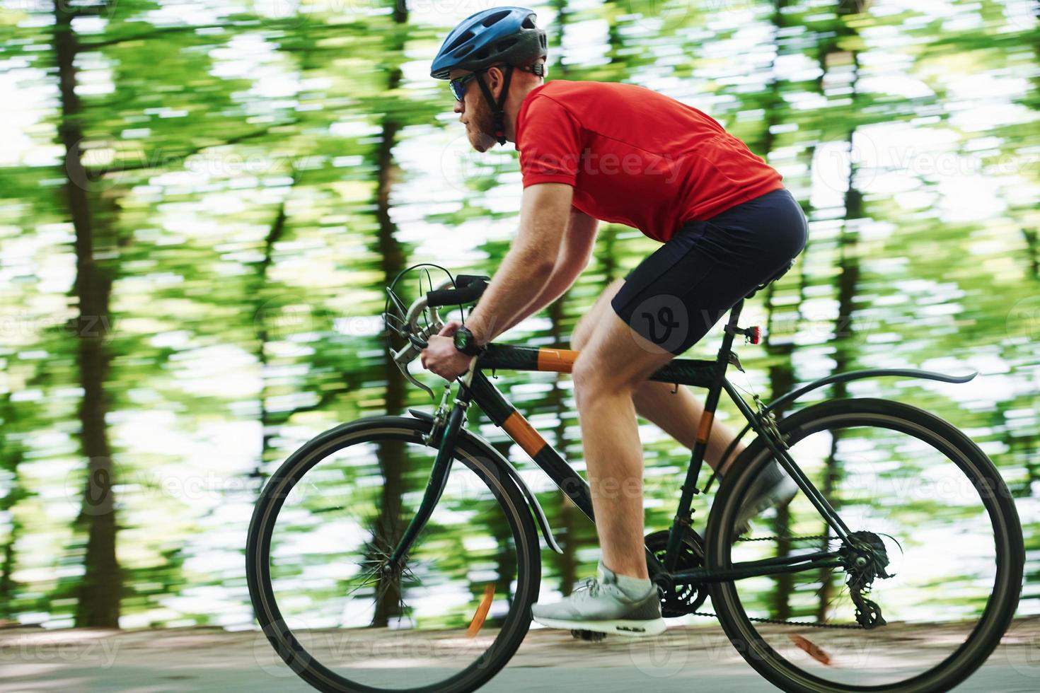 Natural parkland. Cyclist on a bike is on the asphalt road in the forest at sunny day photo