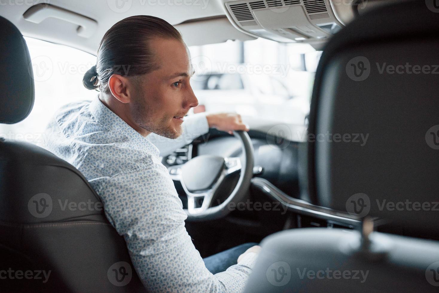 en ropa oficial. hombre probando auto nuevo en el salón durante el día. compra de vehiculo nuevo foto