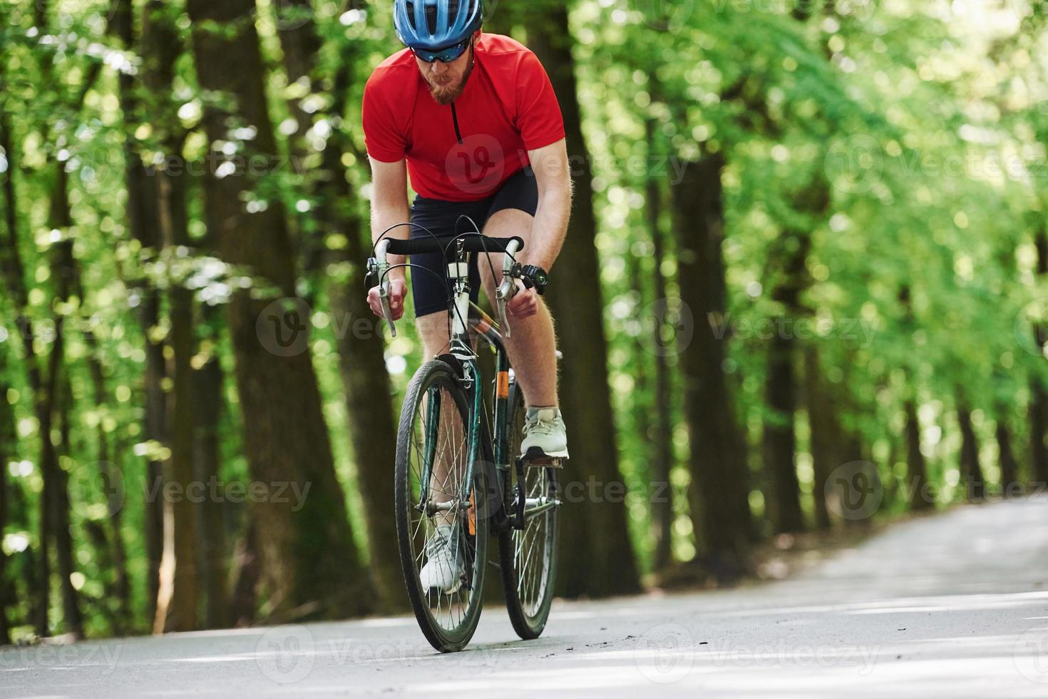 Weekend activities. Cyclist on a bike is on the asphalt road in the forest at sunny day photo