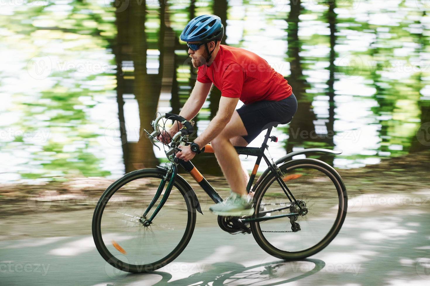 Turing to the left. Cyclist on a bike is on the asphalt road in the forest at sunny day photo