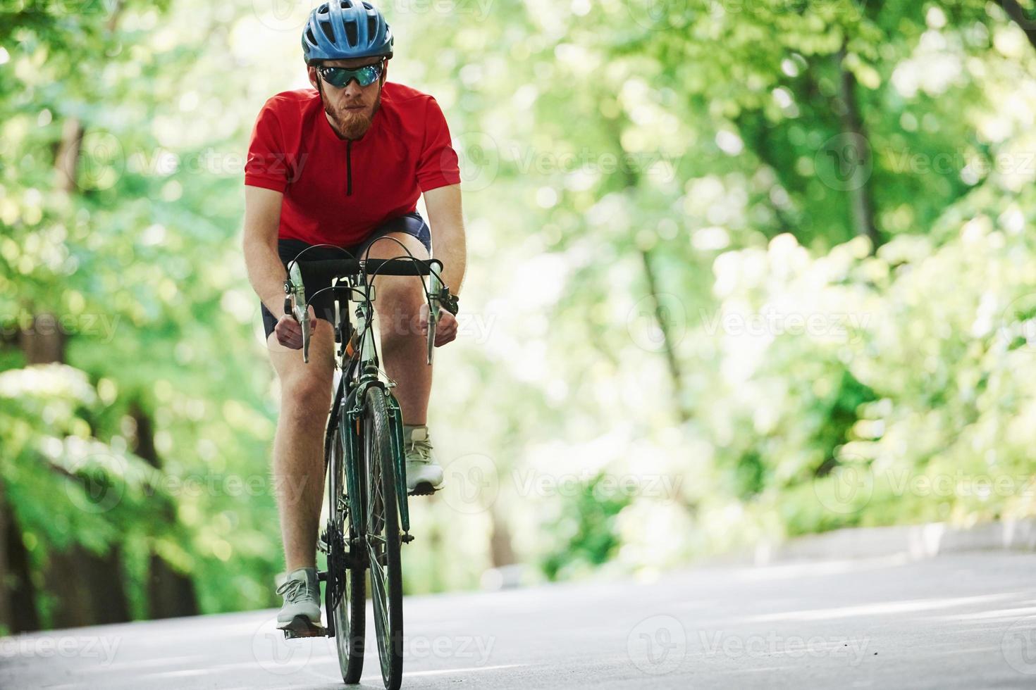 Front view. Cyclist on a bike is on the asphalt road in the forest at sunny day photo
