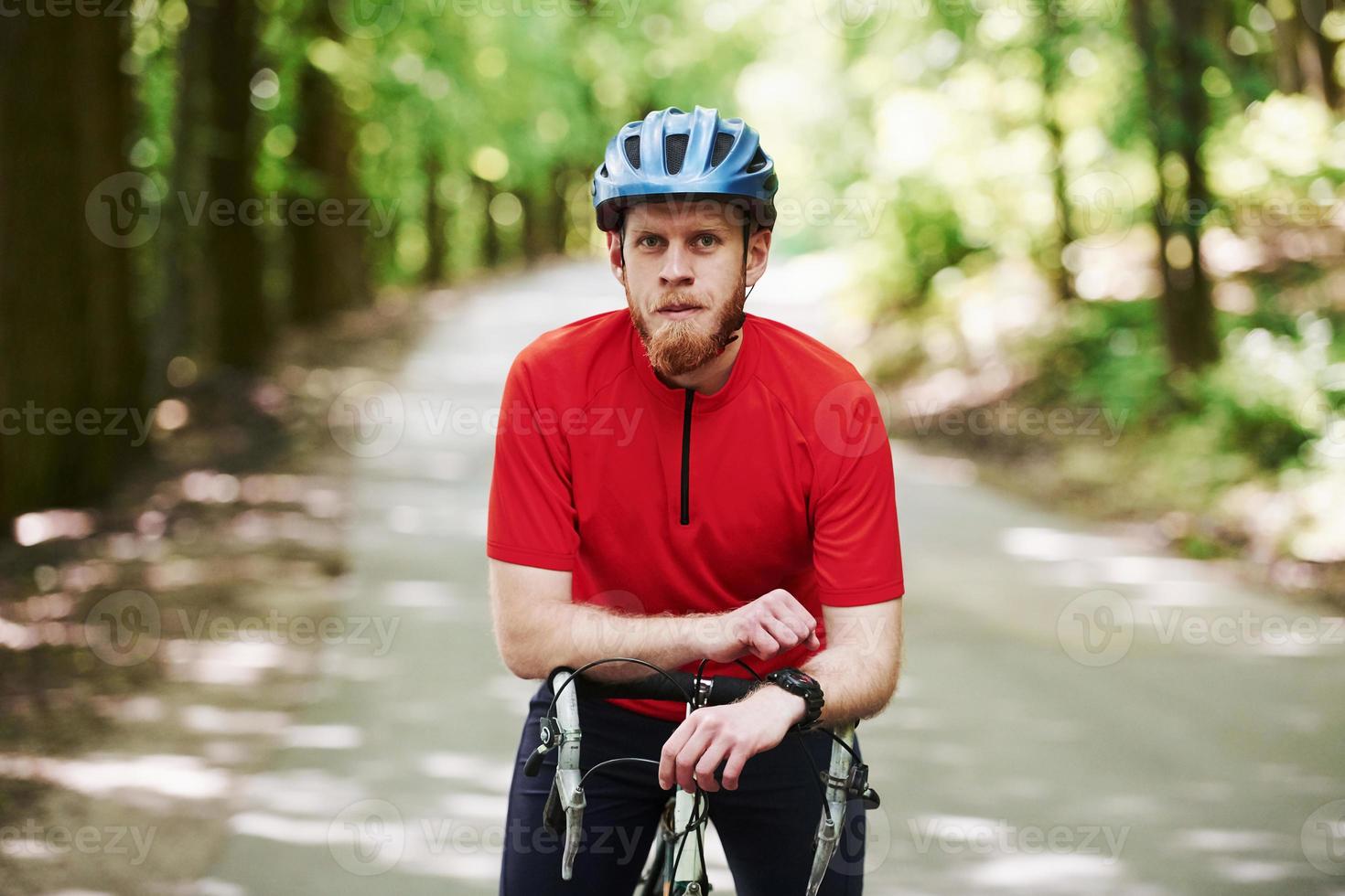 Portrait of bearded man. Cyclist on a bike is on the asphalt road in the forest at sunny day photo