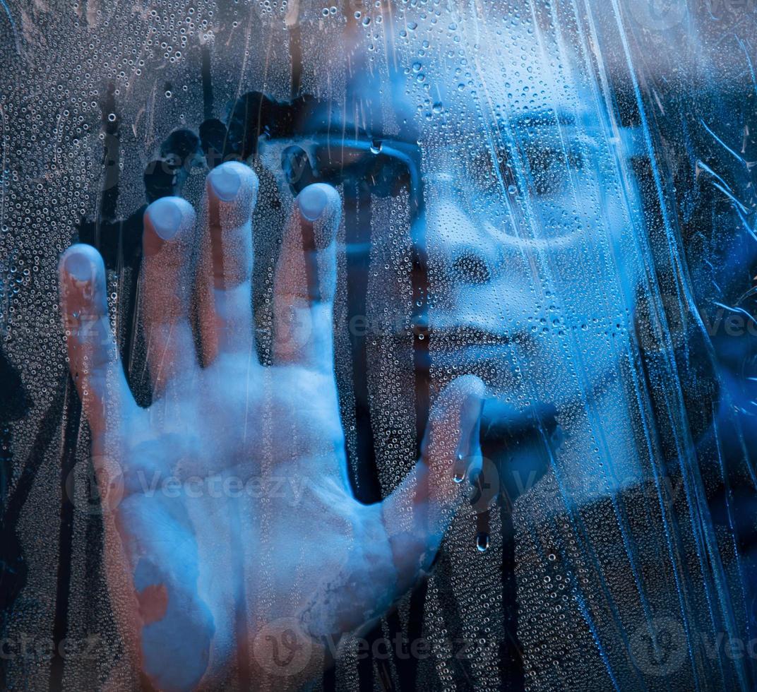 Blue color. Studio shot in dark studio with neon light. Portrait of serious man behind the wet glass photo