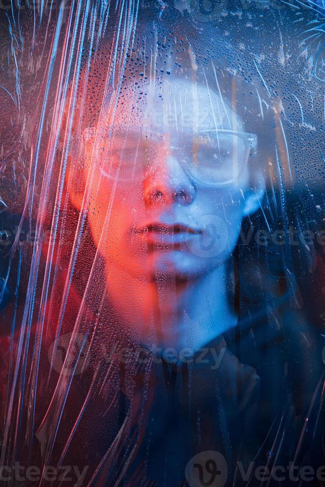 Human face behind the glass. Studio shot in dark studio with neon light. Portrait of serious man behind the wet glass photo