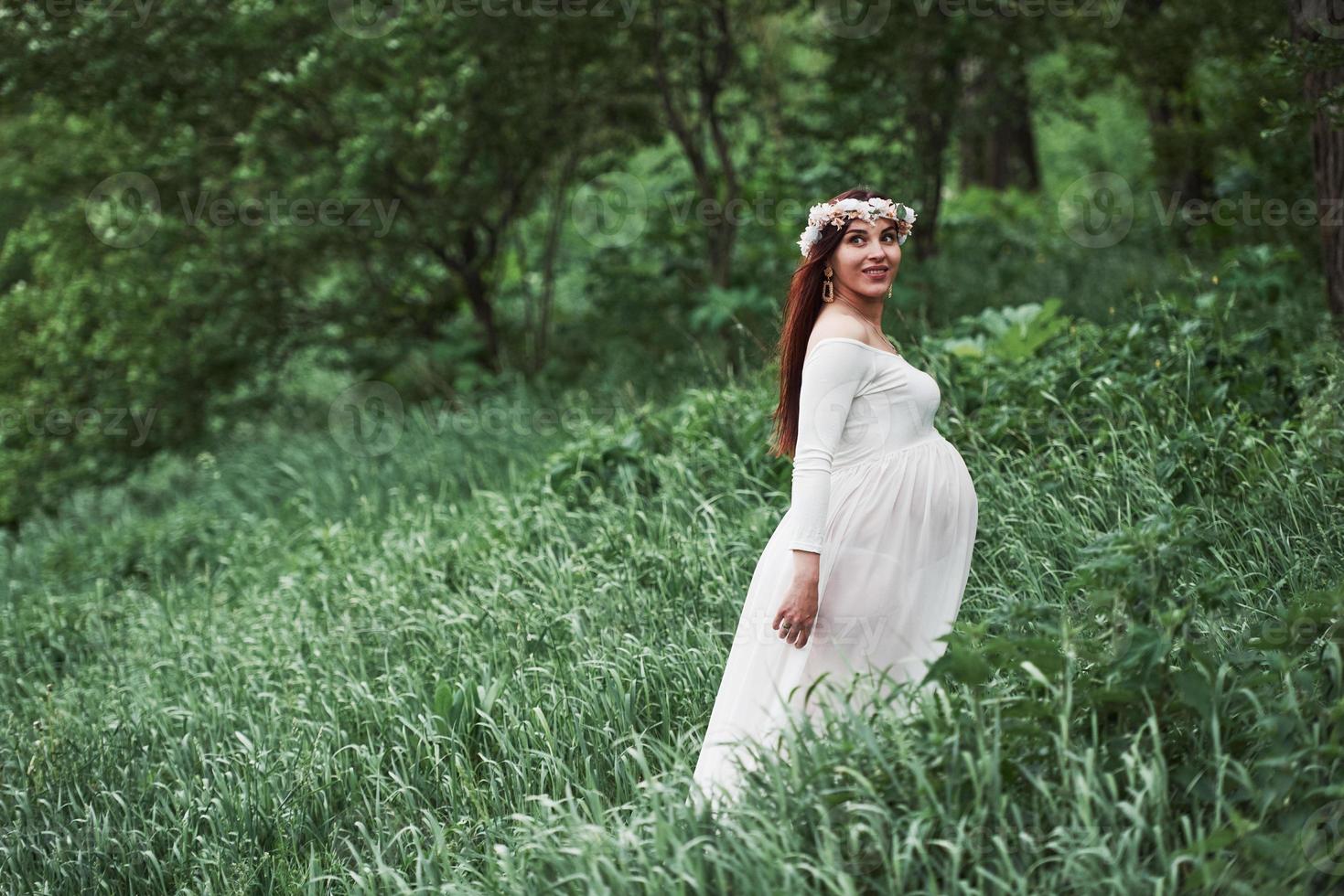In the woods. Beautiful pregnant woman in dress have a walk outdoors. Positive brunette photo