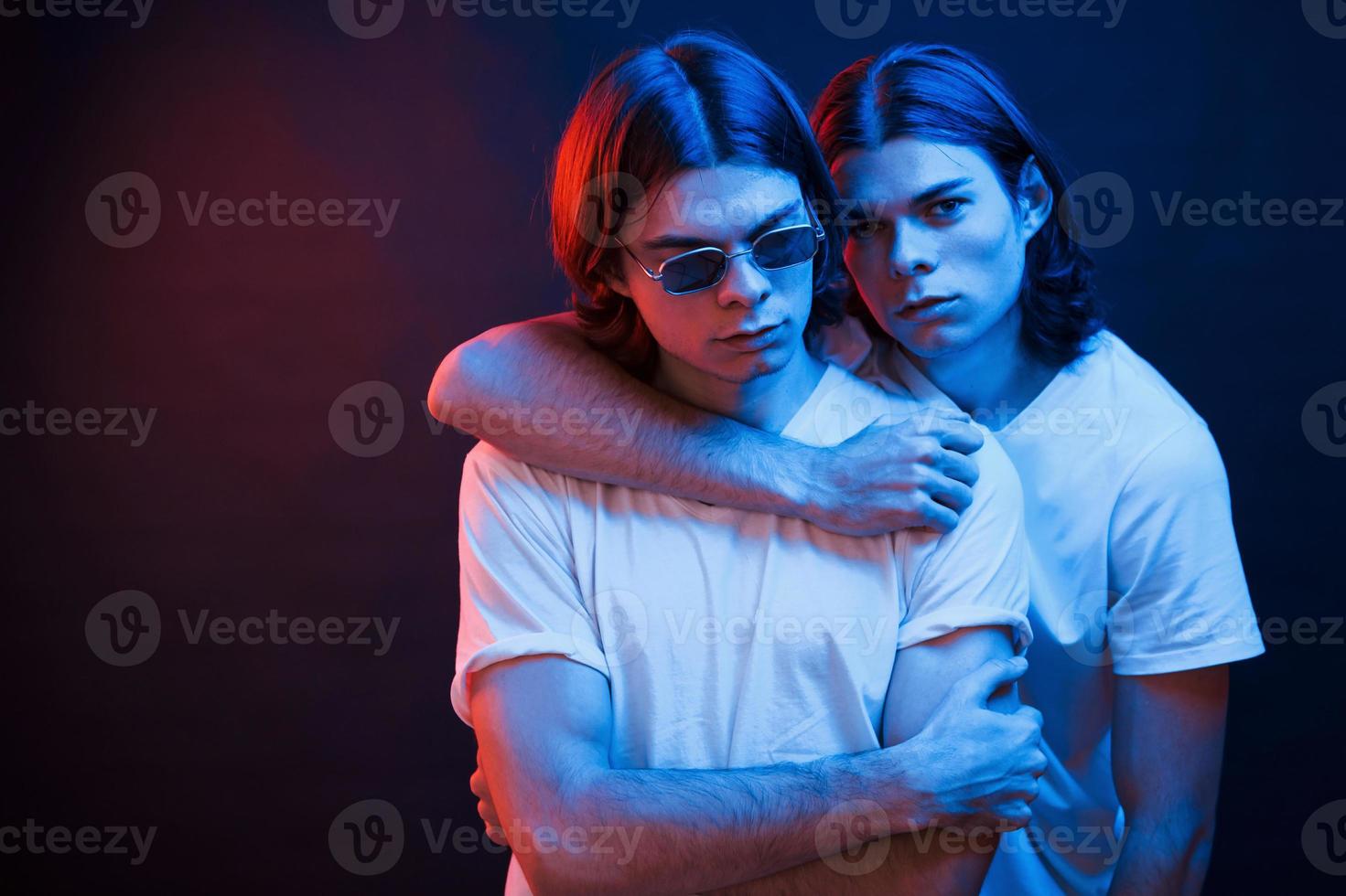 We must be together if we wanna be strong. Portrait of twin brothers. Studio shot in dark studio with neon light photo