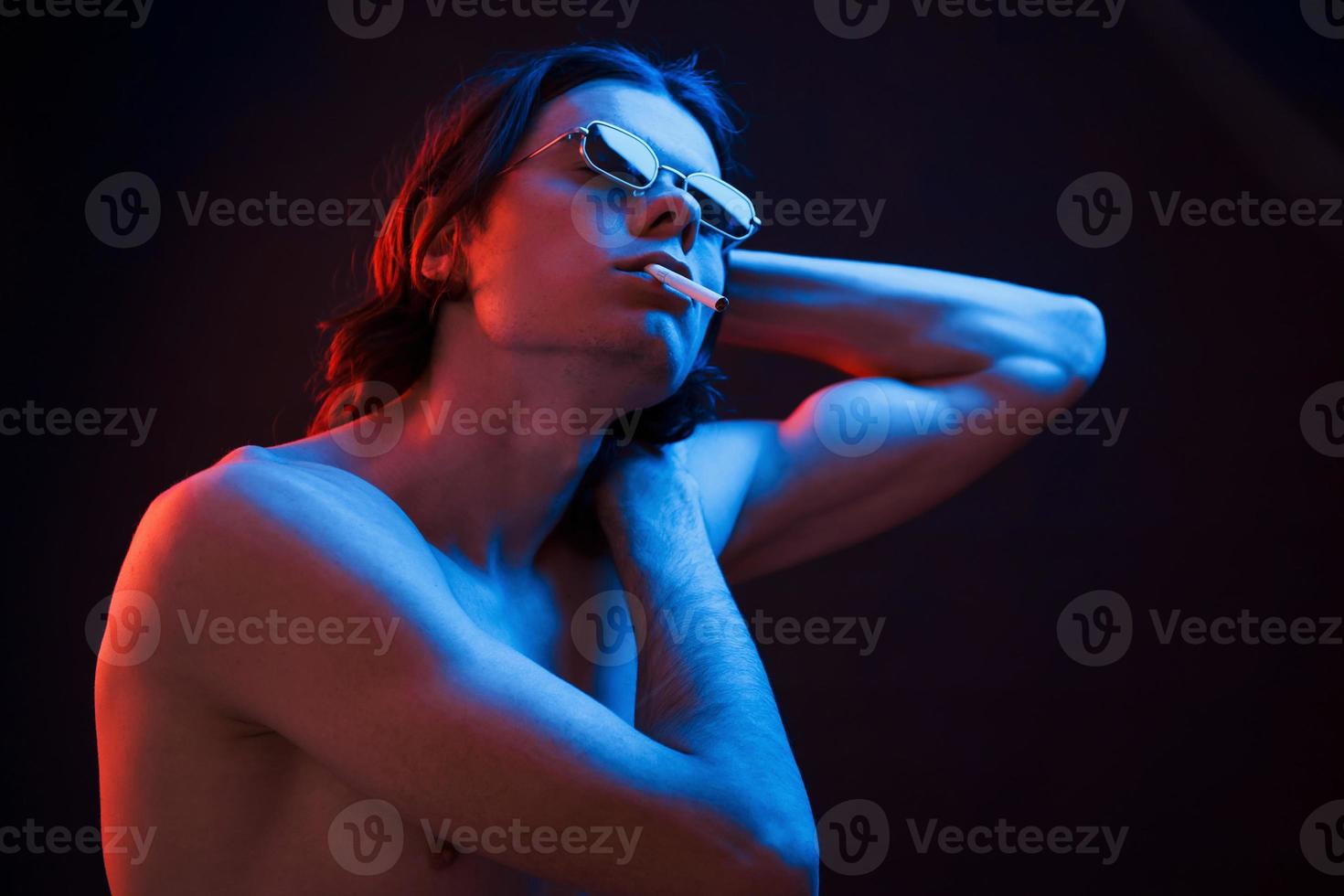 Showing body. Studio shot in dark studio with neon light. Portrait of serious man photo