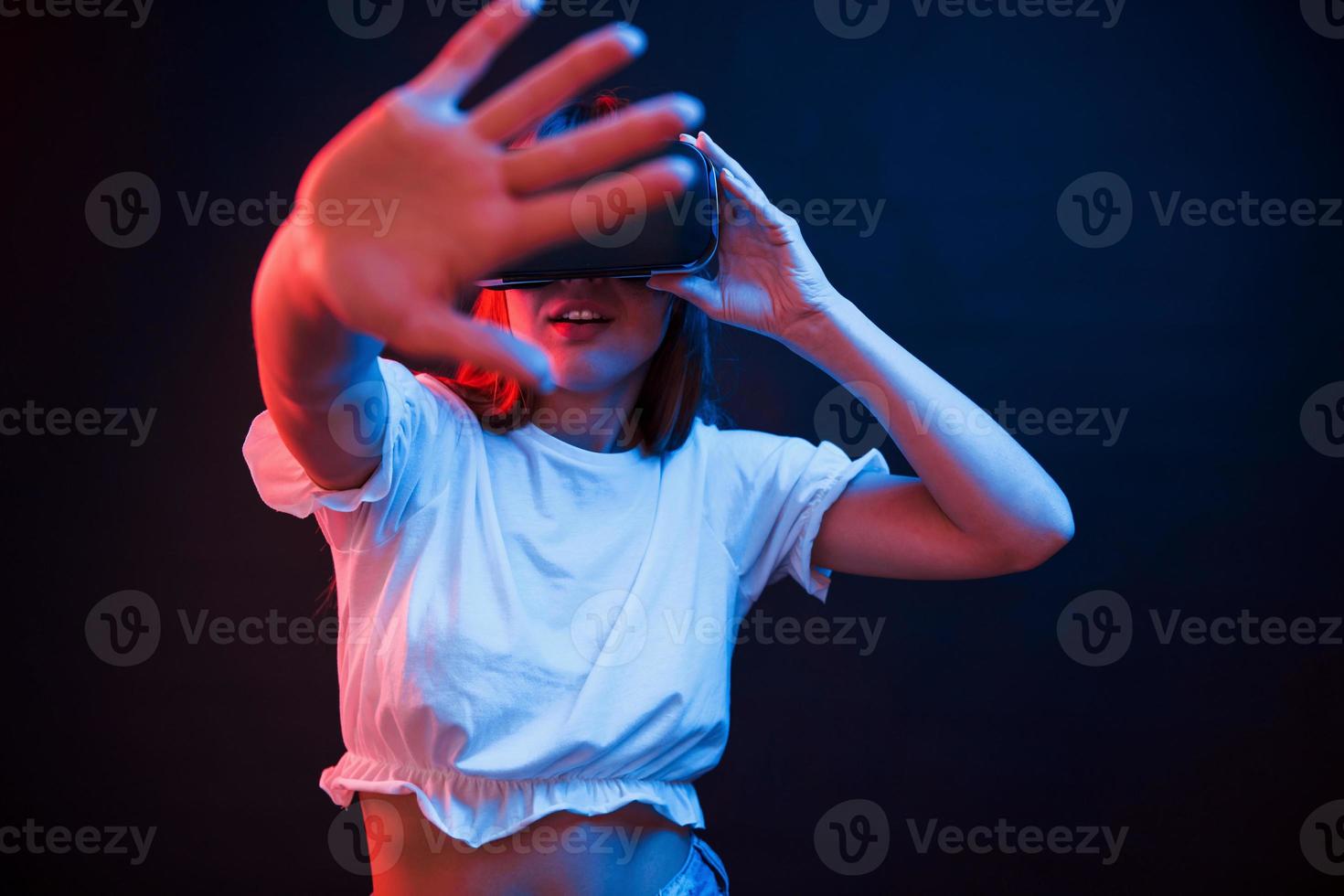 I can see that. Young woman using virtual reality glasses in the dark room with neon lighting photo