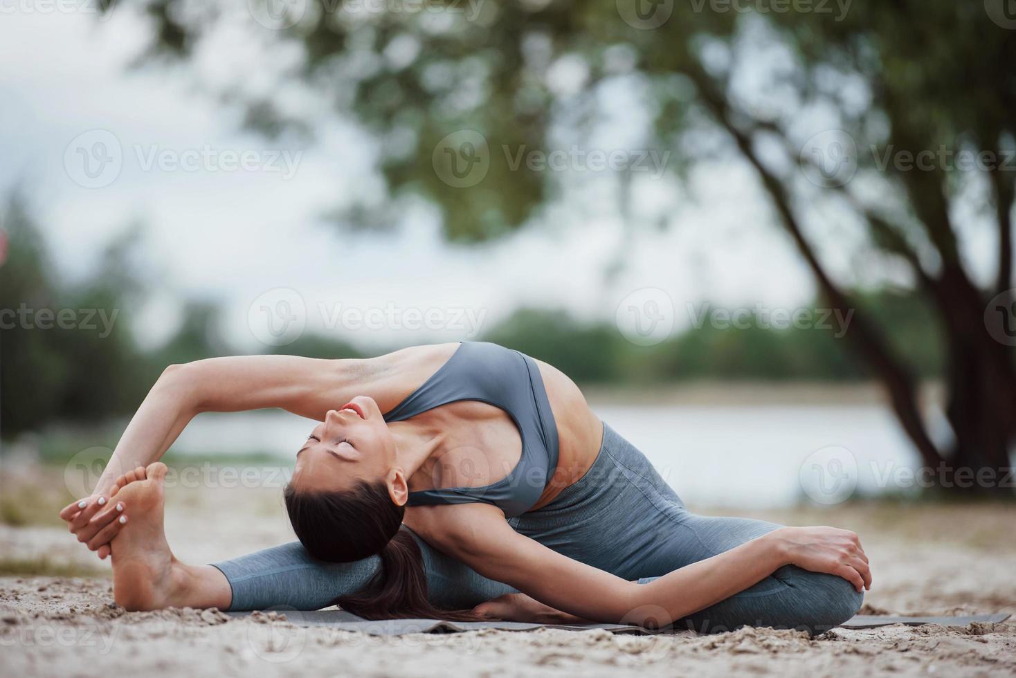 Human flexibility. Brunette with nice body shape in sportive clothes have fitness day on a beach photo