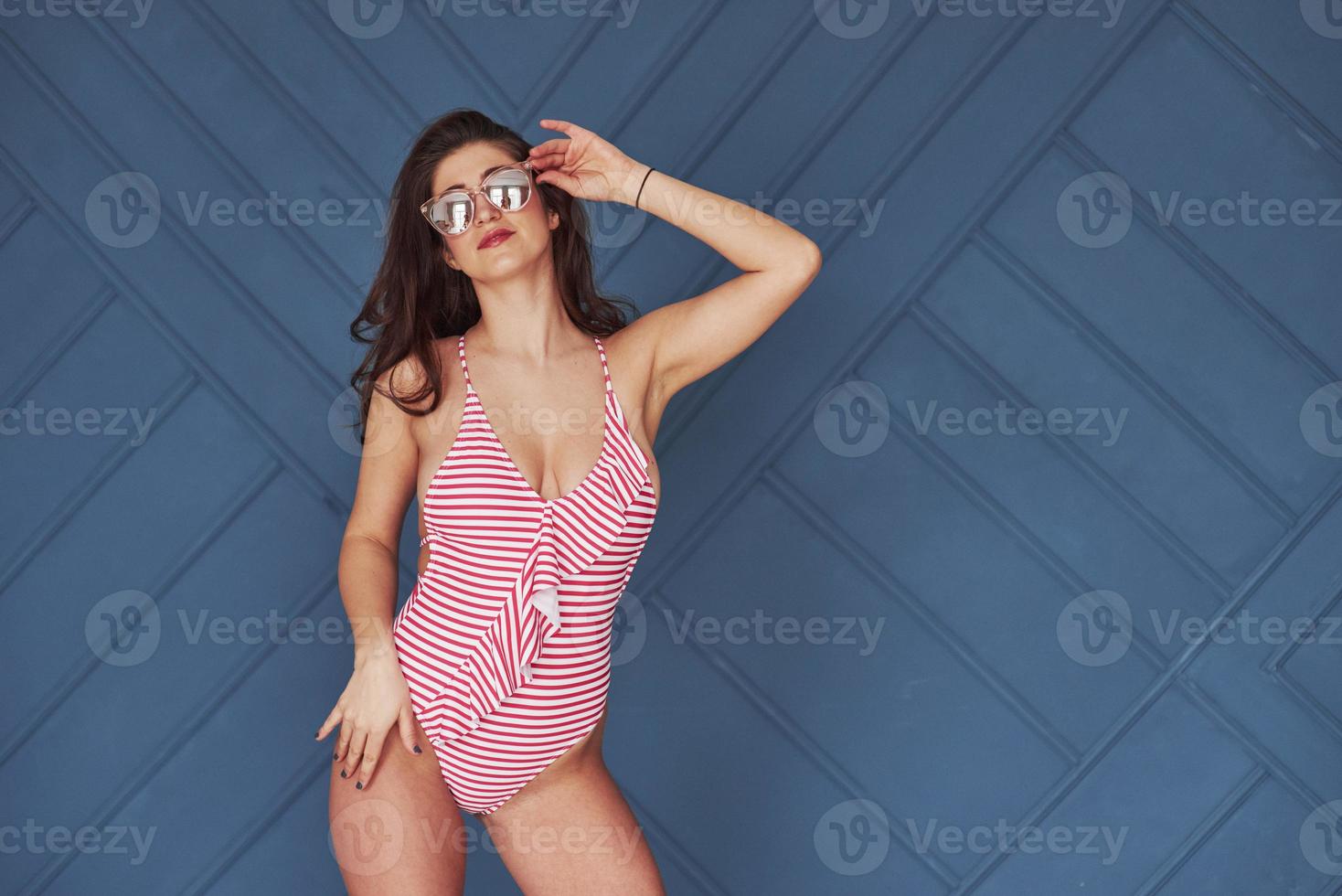 Blue background. Stylish beautiful young girl in bikini stands and posing in the studio photo