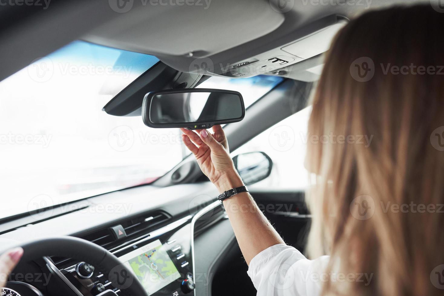 Adjusting the rear view mirror. Close up view of woman's hands in the beautiful modern black colored car photo