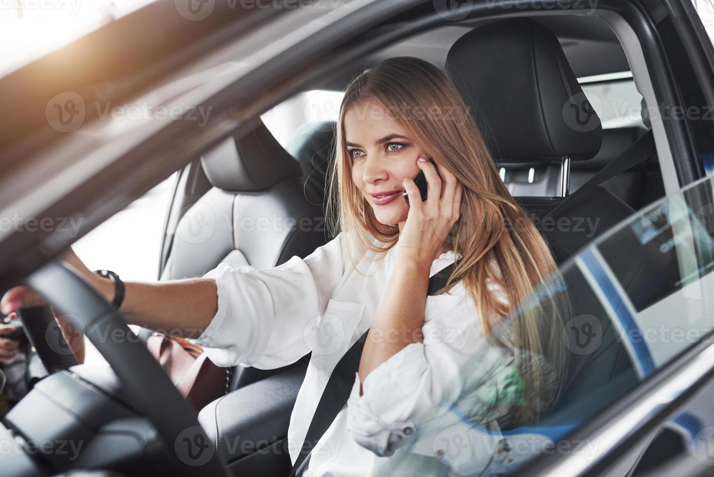 buen rayo de sol sobre el techo. hermosa chica rubia sentada en el auto nuevo con interior negro moderno foto