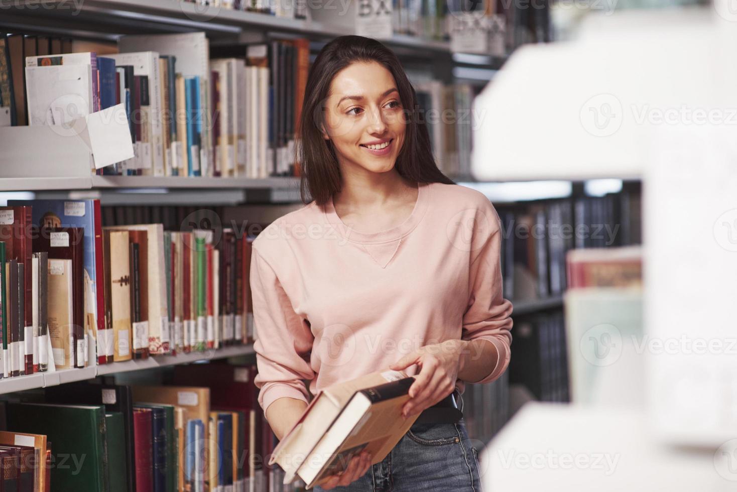 That was I looked for. Brunette girl in casual clothes having good time in the library full of books photo