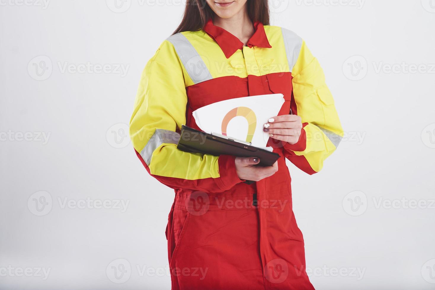 Notepad with diagrams. Brunette woman in orange and yellow uniform stands against white background in the studio photo
