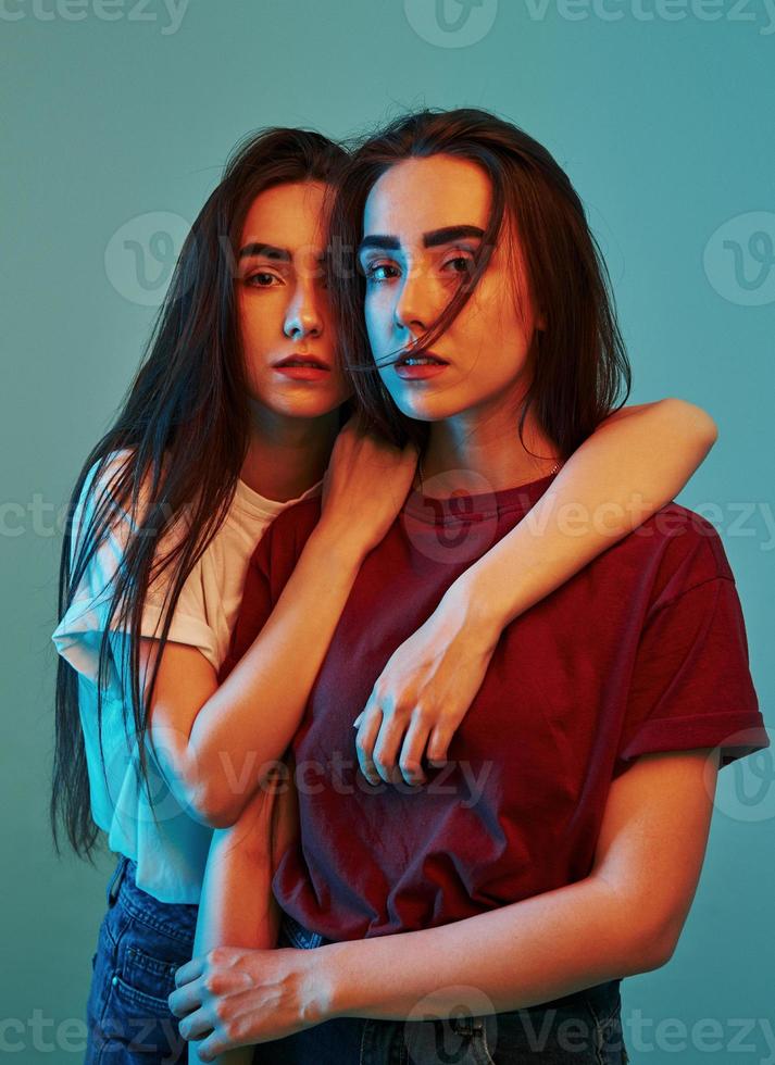 Always together. Studio shot indoors with neon light. Photo of two beautiful twins