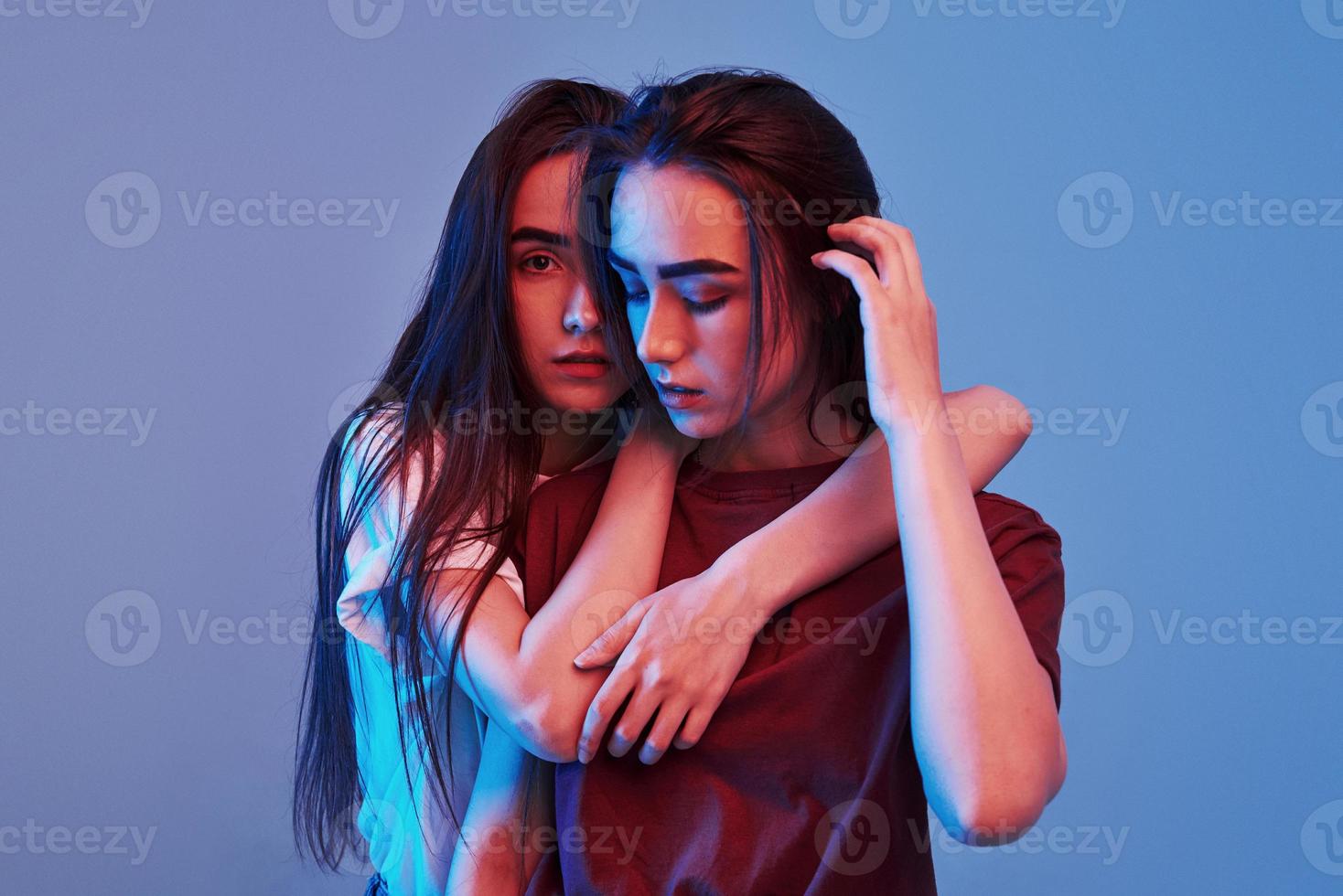 Embracing each other. Studio shot indoors with neon light. Photo of two beautiful twins