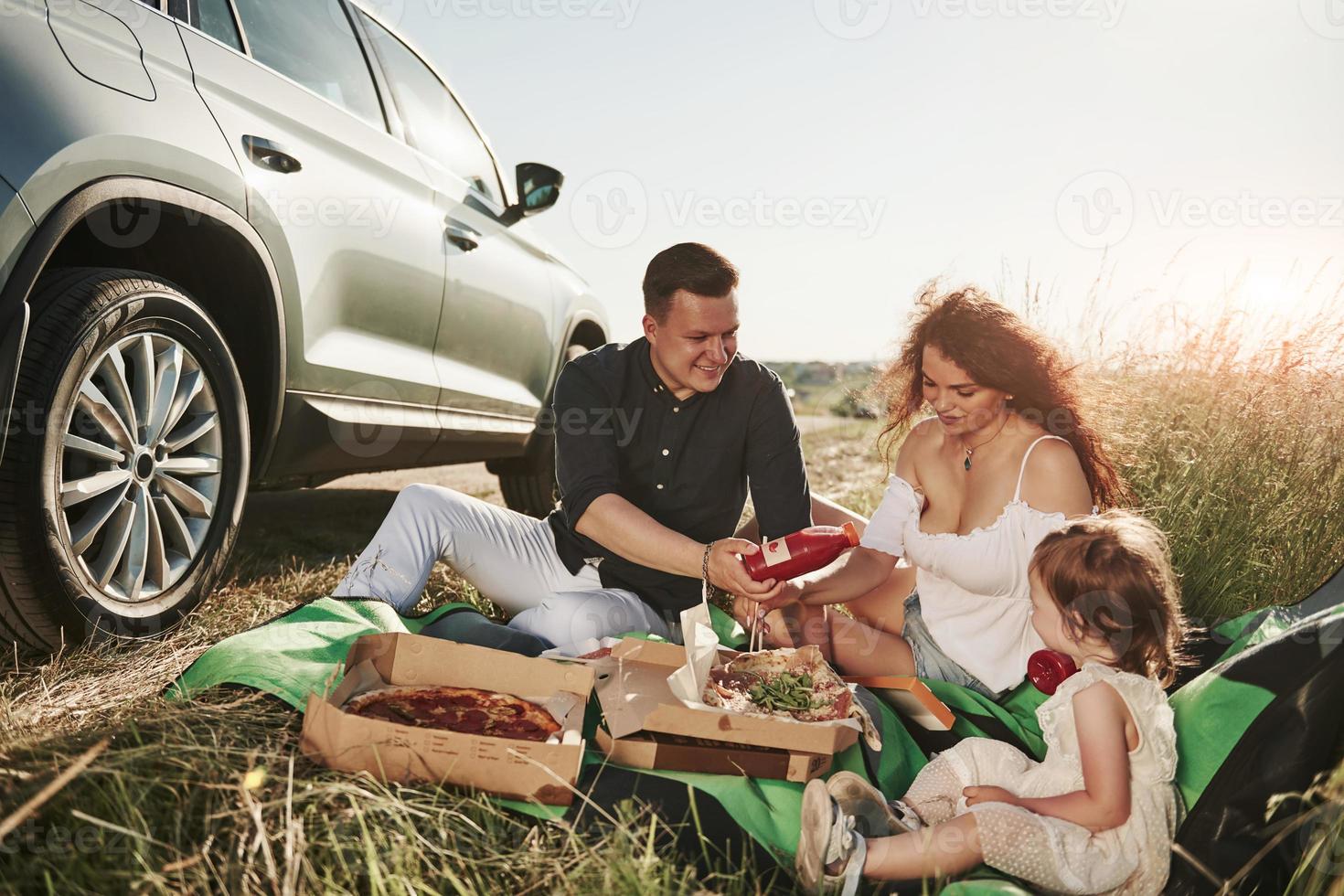 Family have picnic at countryside near silver automobile at sunset photo