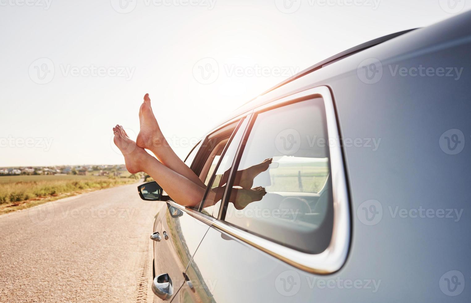 vista lateral. chica pone sus piernas en la ventana del automóvil en el campo foto