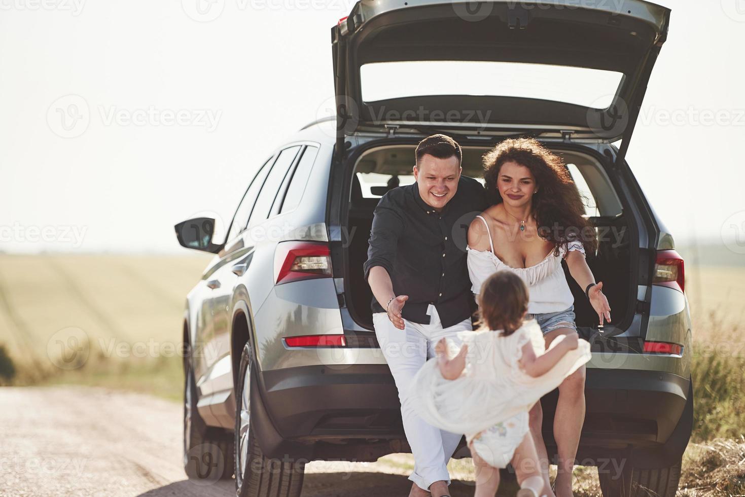 dame abrazos la familia pasa un buen rato en el campo cerca del automóvil plateado al atardecer foto