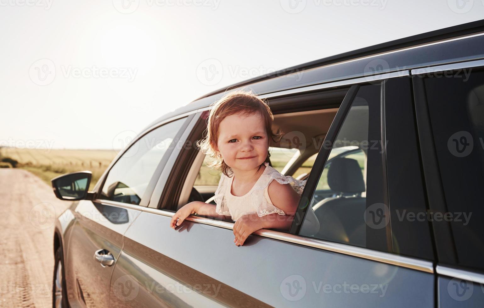 Cute kid looks through the window of brand new modern car at sunny day photo