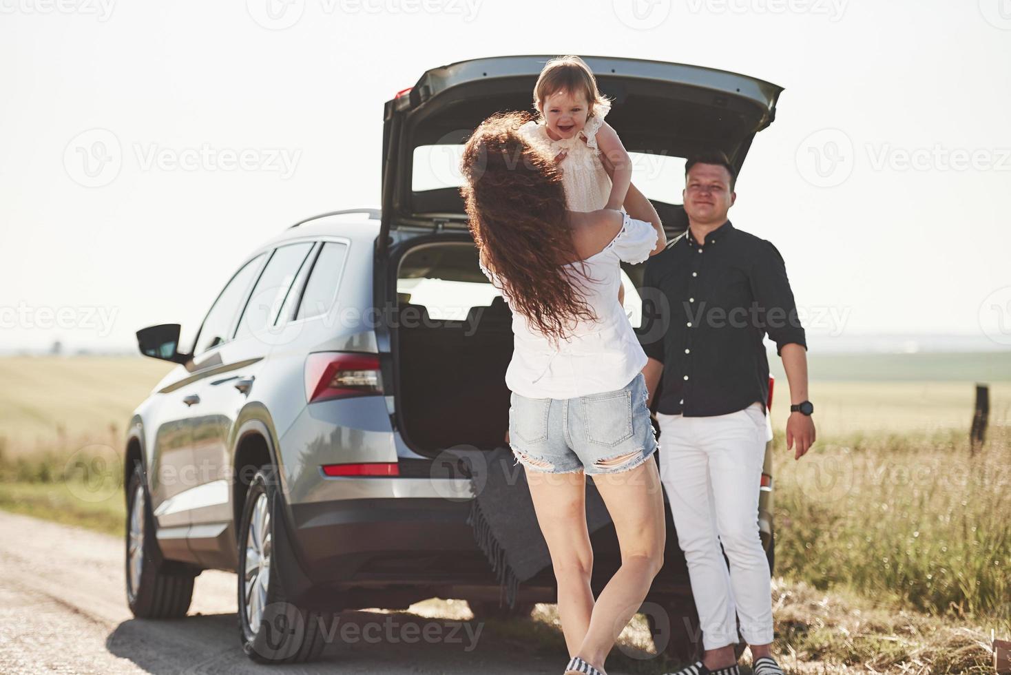 la familia pasa un buen rato en el campo cerca del automóvil plateado al atardecer foto