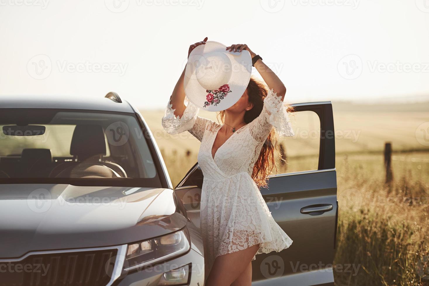 Wearing the hat. Girl in white clothes posing near the modern luxury automobile outdoors photo