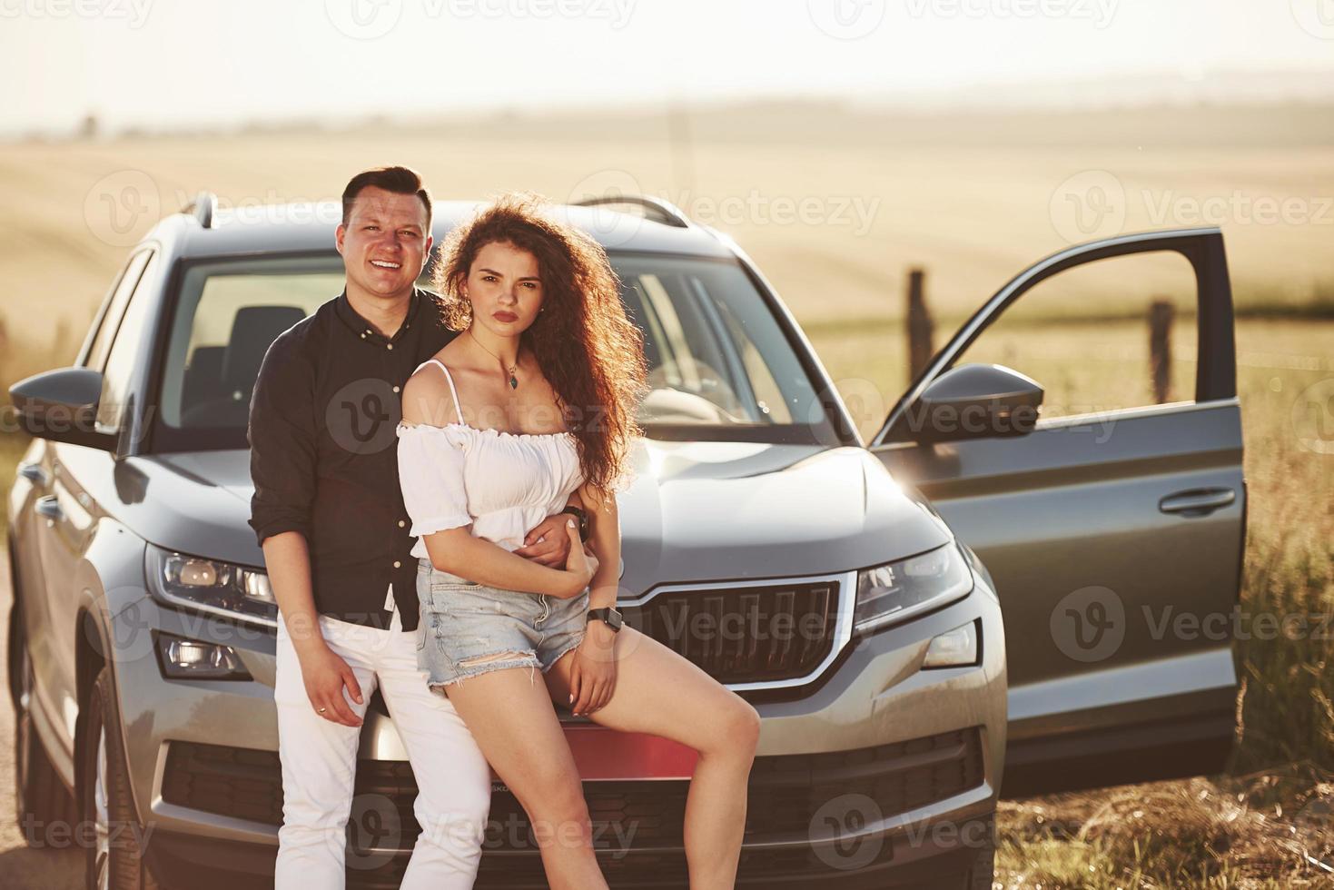 Embracing each other. Lovely couple near their new modern car at weekend time photo