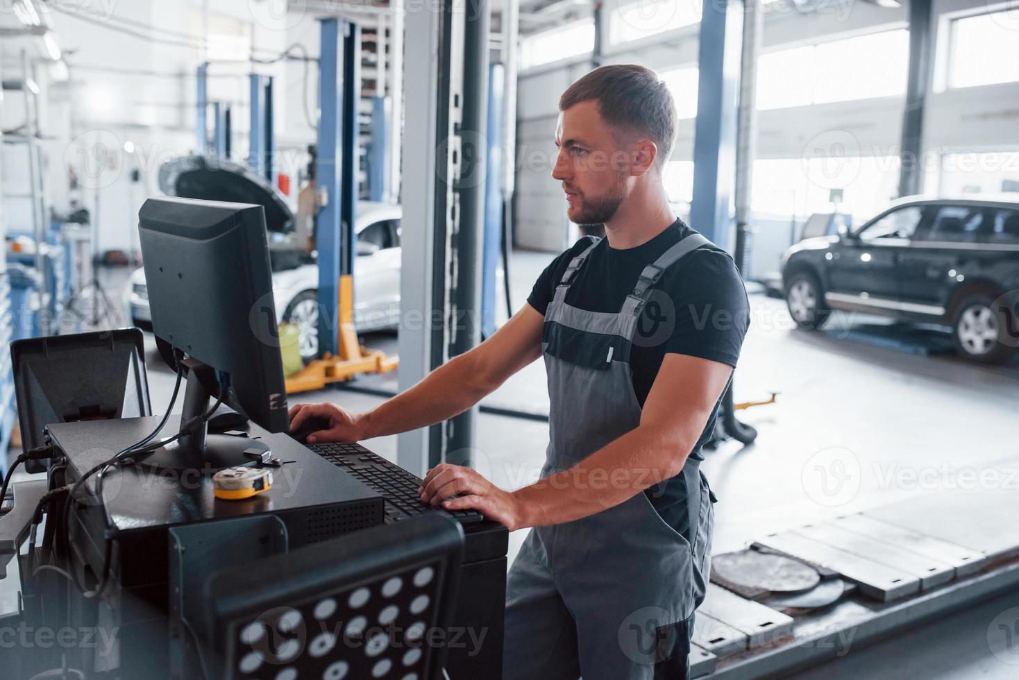 Searching information. Man at the workshop in uniform use computer for his job for fixing broken car photo