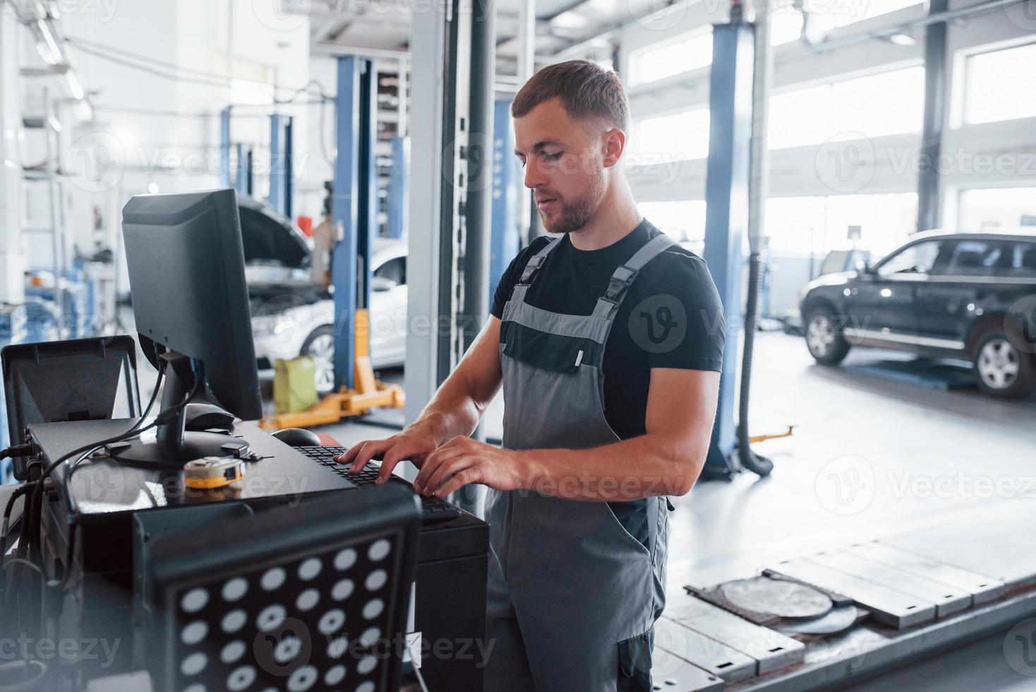 Typing on keyboard. Man at the workshop in uniform use computer for his job for fixing broken car photo