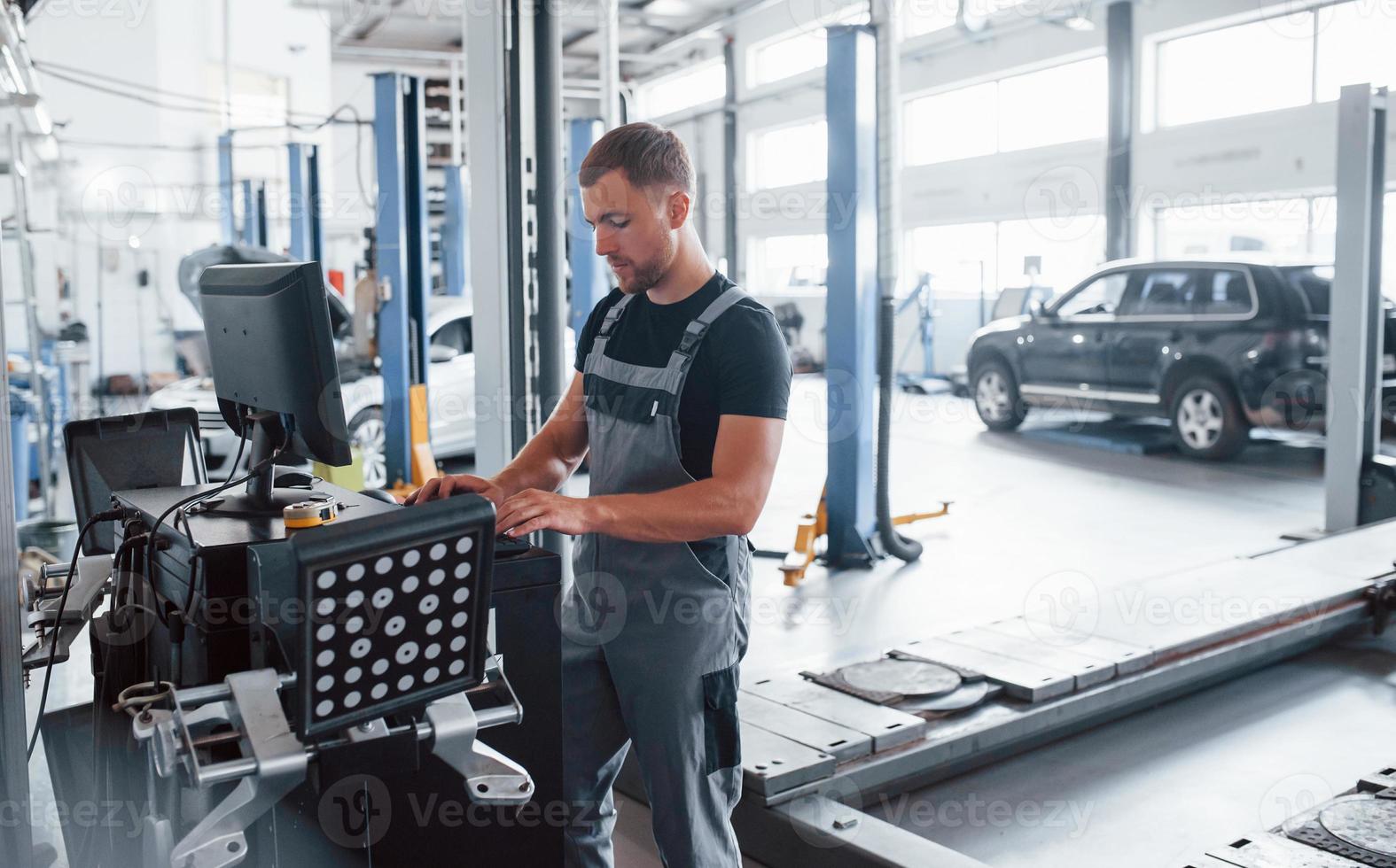 Looks at keyboard. Man at the workshop in uniform use computer for his job for fixing broken car photo