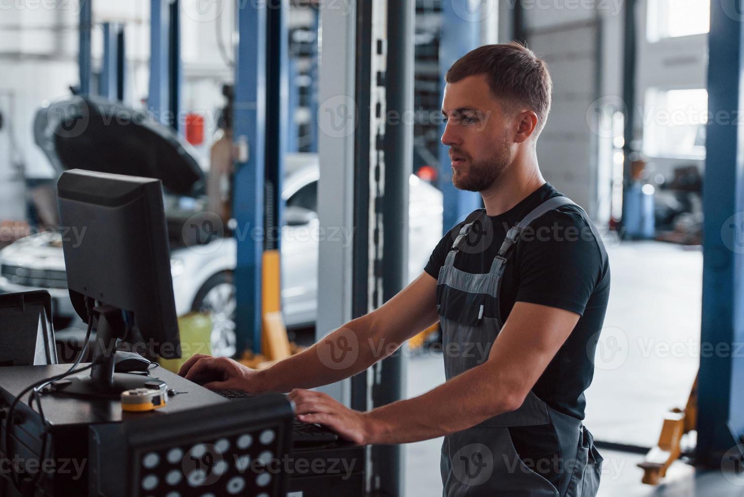 Technologies simplifies life. Man at the workshop in uniform use computer for his job for fixing broken car photo