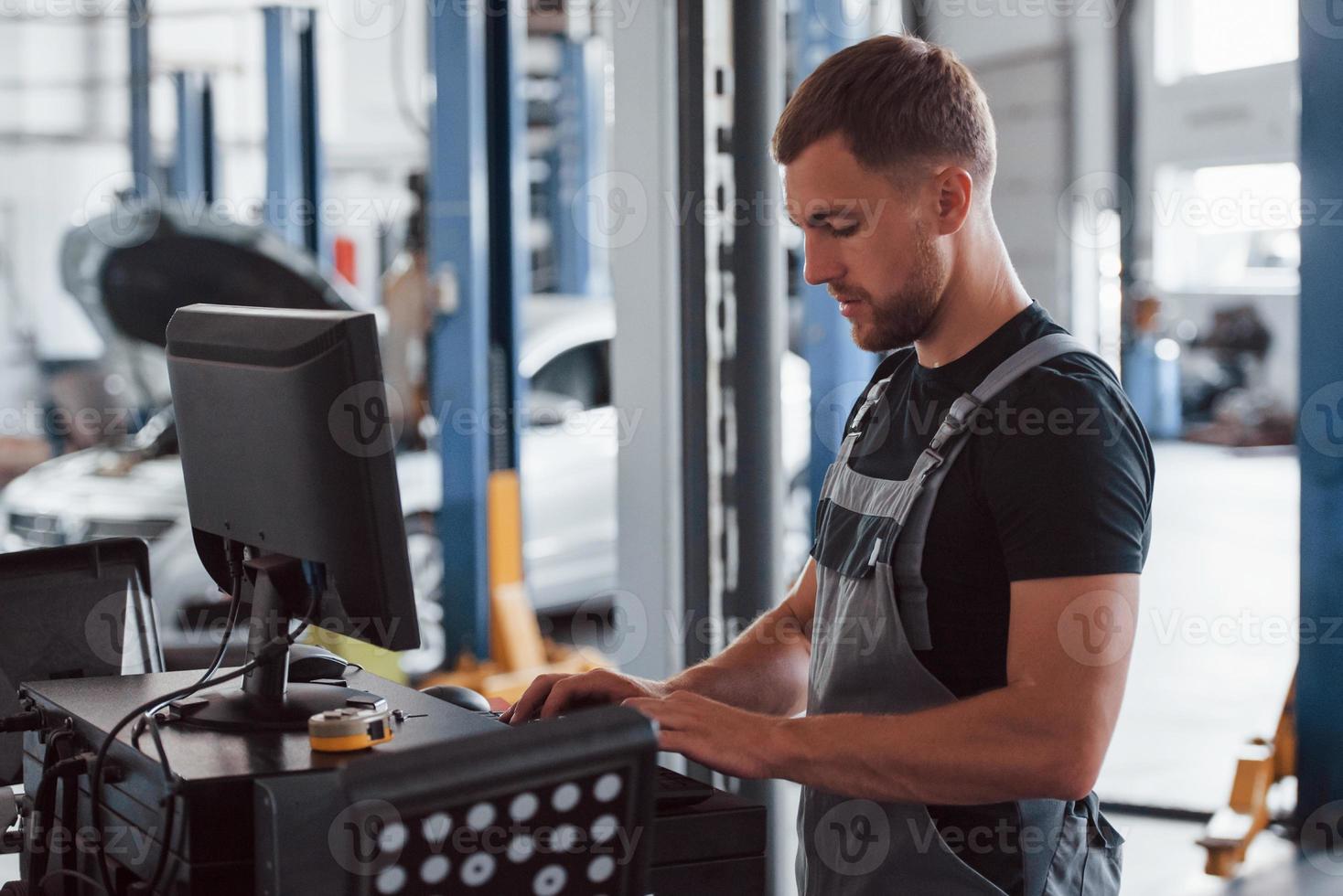 Professional mechanic. Man at the workshop in uniform use computer for his job for fixing broken car photo
