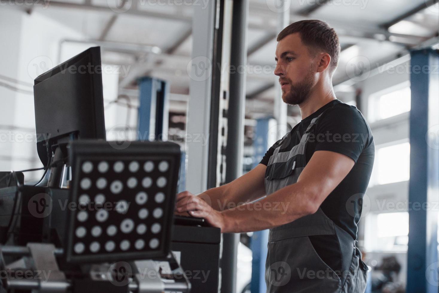 Takes look at monitor. Man at the workshop in uniform use computer for his job for fixing broken car photo