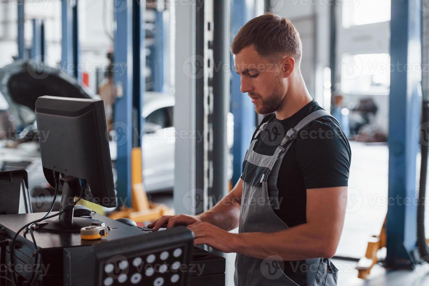 Diagnostic pc. Man at the workshop in uniform use computer for his job for fixing broken car photo